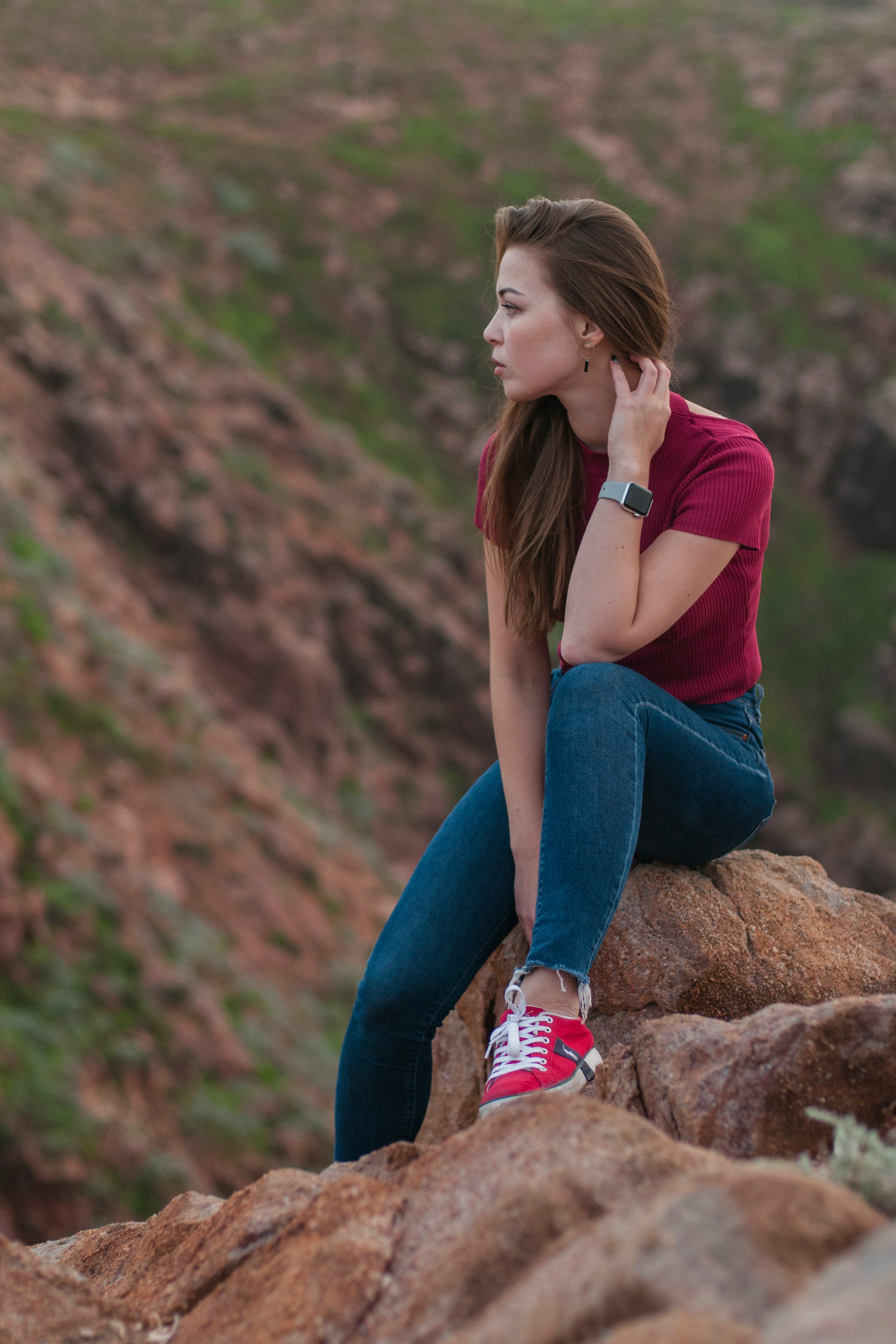 woman in pink shirt and blue denim jeans sitting on brown rock during daytime